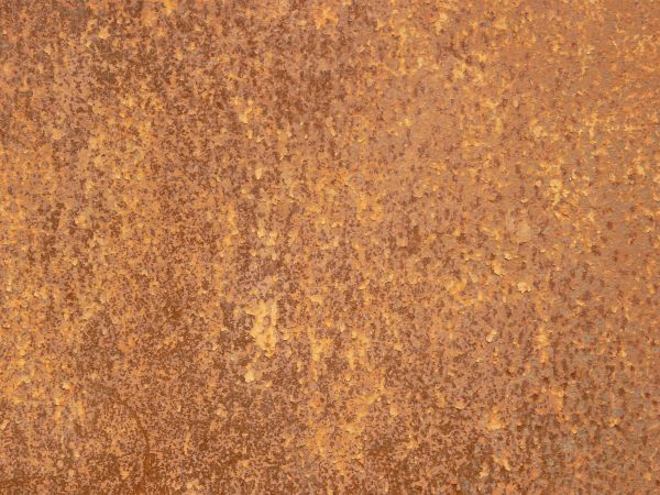 Red rust texture, visible among small flecks of yellow paint and completely covering a a metal surface.